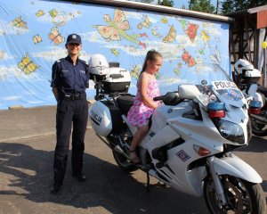 Policjantka w trakcie wydarzenia plenerowego &quot;Emdekolada&quot; na placu Powiatowego Młodzieżowego Domu Kultury i Sportu w Wieluniu. Na motocyklu siedzi dziecko obok stoi umundurowana policjantka