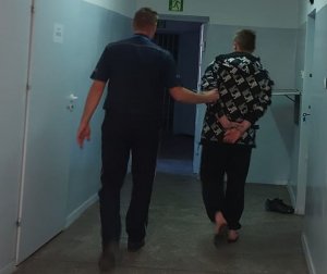 policjant prowadzi zatrzymanego po korytarzu w komendzie