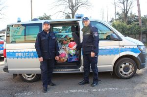 dwójka policjantów stoi przed radiowozem, w którym zapakowane są zabawki zebrane podczas zbiórki