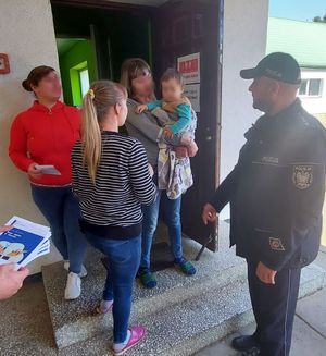 policjant przed budynkiem ośrodka przekazuje informacje  obywatelom Ukrainy w zakresie bezpieczeństwa