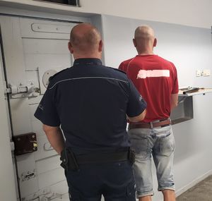 Policjant prowadzi zatrzymanego do celi w pomieszczeniu dla osób zatrzymanych.