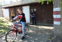 kolorowe zdjęcie przedstawiające policjanta oraz  dzieci pokonujące rowerowy tor przeszkód  na terenie miasteczka ruchu drogowego  podczas  powiatowych eliminacji Turnieju Bezpieczeństwa w Ruchu Drogowym