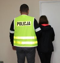 kolorowe zdjęcie ukazujące policjanta w odblaskowej kamizelce z napisem Policja prowadzącego zatrzymaną do kradzieży