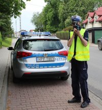 zdjęcie przedstawiające radiowóz i policjanta na drodze dokonującego pomiaru prędkości
