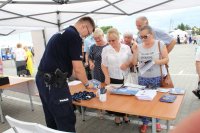 kolorowe zdjęcie przedstawiające stanowisko profilaktyczne na którym policjant rozmawia z uczestnikami Wojewódzkich Dni Seniora na targowisku miejskim w Wieluniu.