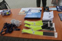 zdjęcie przedstawiające stolik na którym leżą ulotki i broszury informacyjne, elementy odblaskowe  oraz smycze i długopisy
