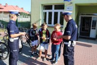 umundurowani policjanci ruchu drogowego wręczają dzieciom odblaski przed szkołą