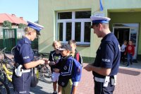 umundurowani policjanci ruchu drogowego wręczają dzieciom odblaski przed szkołą