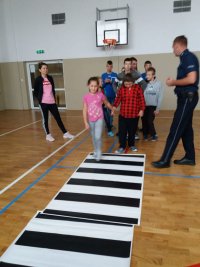 policjant uczy dzieci jak prawidłowo przechodzić przez  przejście dla pieszych  w trakcie spotkania edukacyjno- profilaktycznego