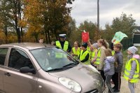 zdjęcie przedstawiające policjanta, dzieci ze szkoły podstawowej oraz kierującego zatrzymanego do kontroli w trakcie akcji &quot;Jabłko Cytryna&quot;