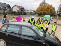 zdjęcie przedstawiające policjanta, dzieci ze szkoły podstawowej oraz kierującego zatrzymanego do kontroli w trakcie akcji jabłko-cytryna