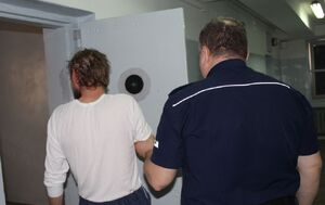 policjant prowadzący zatrzymanego do pomieszczenia dla osób zatrzymanych