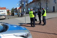 policjanci przy przejściu dla pieszych rozmawiają z przechodniami na temat bezpieczeństwa niechronionych uczestników ruchu drogowego wręczając odblaski