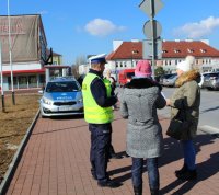 policjanci przy przejściu dla pieszych rozmawiają z przechodniami na temat bezpieczeństwa niechronionych uczestników ruchu drogowego wręczając odblaski