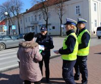 policjanci przy przejściu dla pieszych rozmawiają z przechodniami na temat bezpieczeństwa niechronionych uczestników ruchu drogowego wręczając odblaski