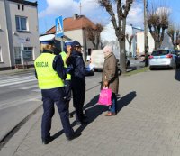 policjanci przy przejściu dla pieszych rozmawiają z przechodniami na temat bezpieczeństwa niechronionych uczestników ruchu drogowego wręczając odblaski