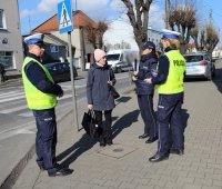 policjanci przy przejściu dla pieszych rozmawiają z przechodniami na temat bezpieczeństwa niechronionych uczestników ruchu drogowego wręczając odblaski