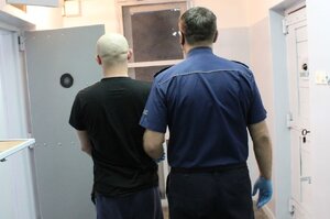 policjant prowadzi zatrzymanego do celi w PDOZ