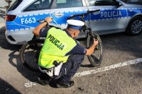 umundurowany policjant sprawdzający numer seryjny roweru. W tle stoi oznakowany radiowóz.