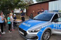 radiowóz stojący w tle oraz policjantka na Jesiennym Pikniku, która przeprowadza quiz wiedzy o bezpieczeństwie wśród uczestników. Całość imprezy odbywa się na na powietrzu.