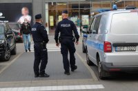 patrol dwóch umundurowanych policjantów sprawdza przy galerii handlowej stosowanie się mieszkańców do obostrzeń w związku z zapobieganiem rozprzestrzenianiu się covid 19