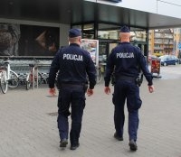 patrol dwóch umundurowanych policjantów sprawdza przy  markecie stosowanie się mieszkańców do obostrzeń w związku z zapobieganiem rozprzestrzenianiu się covid 19