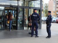 patrol dwóch umundurowanych policjantów sprawdza przy  markecie stosowanie się mieszkańców do obostrzeń w związku z zapobieganiem rozprzestrzenianiu się covid 19