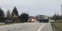 służby ratownicze pracujące na drodze gdzie doszło do wypadku, wóz strażacki, policjanci, strażacy oraz w tle widoczny samochód ciężarowy który uczestniczył w zdarzeniu
