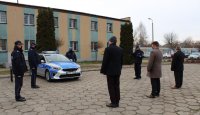 na parkingu przed budynkiem komendy policji stoi zaparkowany radiowóz , na zdjęciu widoczni są również  policjanci i zaproszeni goście.