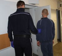 umundurowany policjant prowadzi zatrzymanego do policyjnej celi