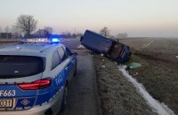 zdjęcie przedstawiające drogę , oznakowany radiowóz policyjny i samochód dostawczy, który leży przewrócony a bok w rowie.