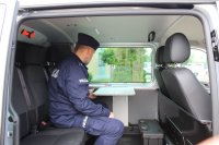 oznakowany radiowóz stoi zaparkowany przed wieluńską komendą, w aucie siedzi  umundurowany policjant prezentujący wyposażenie radiowozu