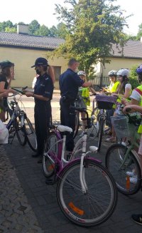 umundurowani policjanci  w trakcie spotkania profilaktycznego przez rajdem rowerowym wśród uczestniczących w nim uczniów ze szkoły.