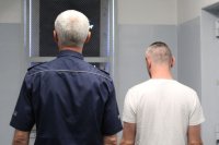 umundurowany policjant prowadzi zatrzymanego do celi