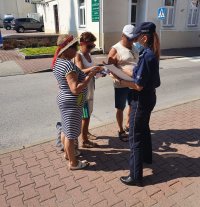 policjantka wręcza przechodniom ulotki ostrzegające przed oszustwami