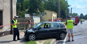 policjanci pracujący na miejscu zdarzenia. Na pierwszym planie rozbity samochód uczestniczący w zdarzeniu.