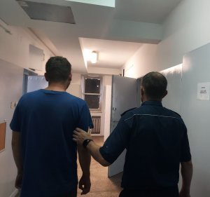 policjant prowadzi zatrzymanego po korytarzu w pomieszczeniu dla osób zatrzymanych
