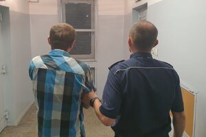 umundurowany policjant prowadzi zatrzymanego w pomieszczeniach policyjnego aresztu
