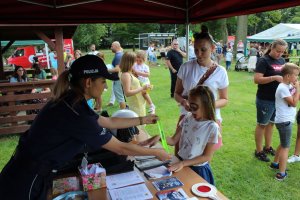 policjantka na stoisku profilaktycznym wręcza dzieciom odblaski