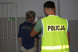 policjant w kamizelce odblaskowej z napisem policja prowadzi zatrzymanego po korytarzu wieluńskiej komendy