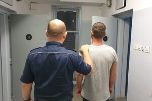 umundurowany policjant prowadzi zatrzymanego po korytarzu w policyjnym areszcie
