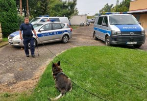 przewodnik psa służbowego wraz z czworonogiem prowadzi pokaz przed budynkiem komendy