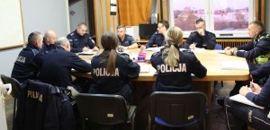 umundurowani policjanci siedzą przy stole podczas odprawy do służby z Naczelnikiem Wydziału Ruchu Drogowego