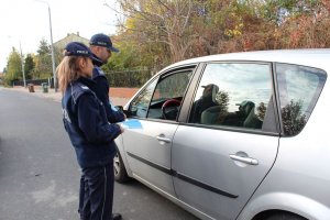 umundurowani policjanci wręczają kierowcy auta zawieszkę zapachową i odblask