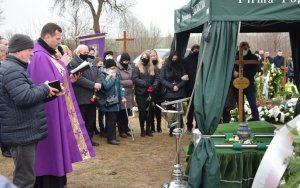 na cmentarzu duchowny odmawia modlitwę przy prochach zmarłego, wokół zgromadzeni uczestnicy uroczystości pogrzebowej