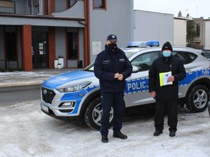 policjant na tle radiowozu z seniorem trzymającym kamizelkę odblaskową i ulotkę do zdjęcia