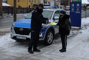 policjant na tle radiowozu wręcza seniorce kamizelkę odblaskową i ulotkę