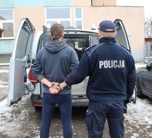 policjant prowadzi zatrzymanego w kajdankach do radiowozu