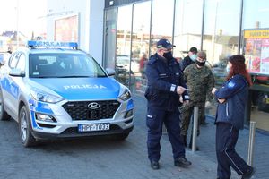 policjanci przed sklepem rozdają elementy odblaskowe i zawieszki zapachowe przechodniom