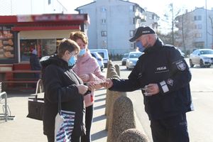 policjant przed sklepem rozdają elementy odblaskowe i zawieszki zapachowe przechodniom